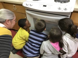 children looking into oven window as adult looks in over their shoulders