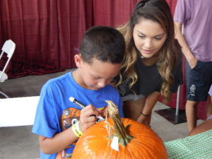 Youth volunteer helping child decorate pumpkin at fair